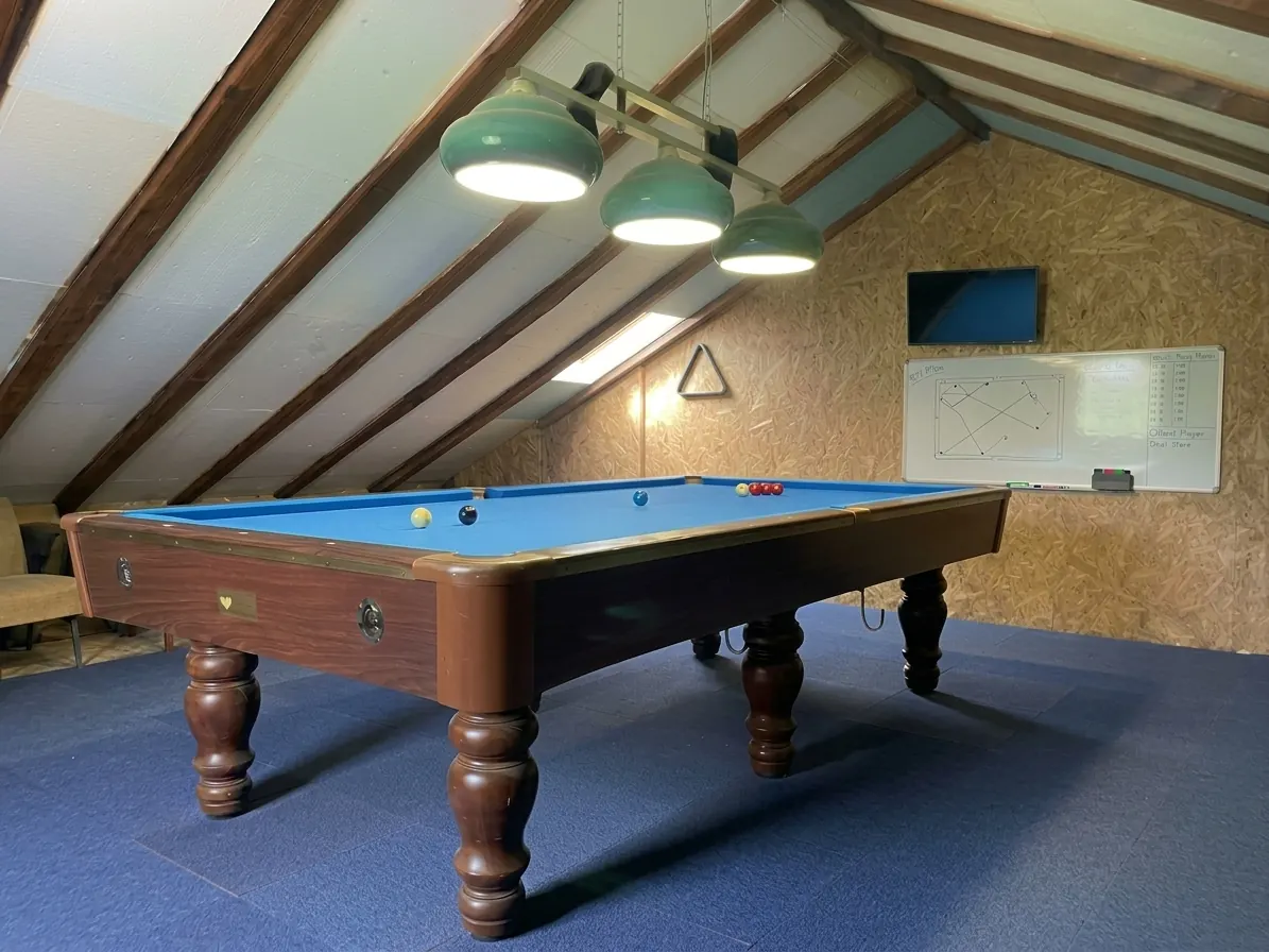 Attic games room with a pool table, green lamps and a whiteboard
