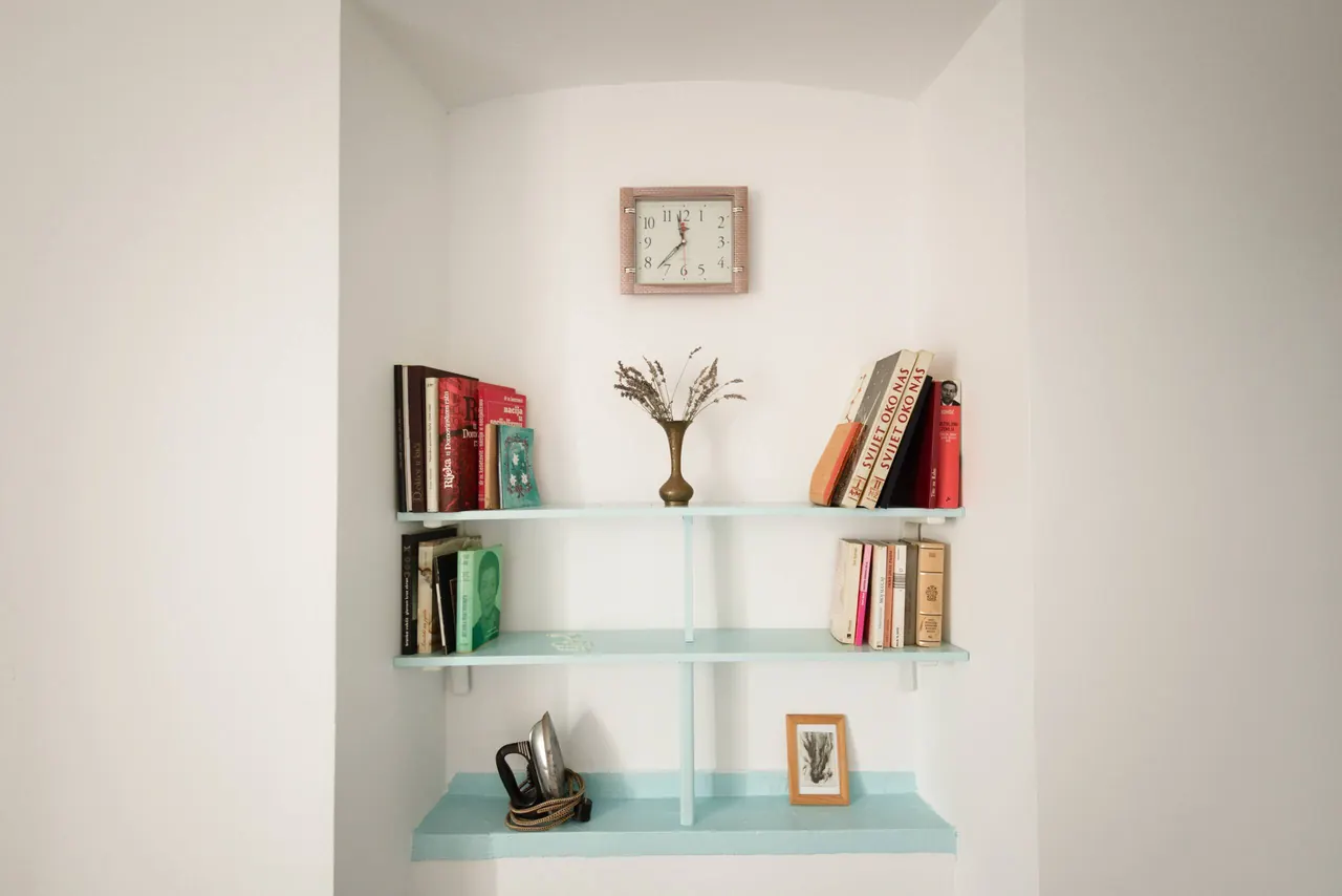 Mint-green wall shelves with books, a clock and dried flowers