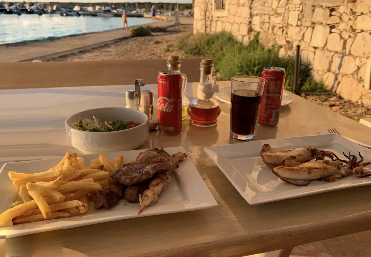 Grilled squid and meat with fries on a table by the beach at sunset