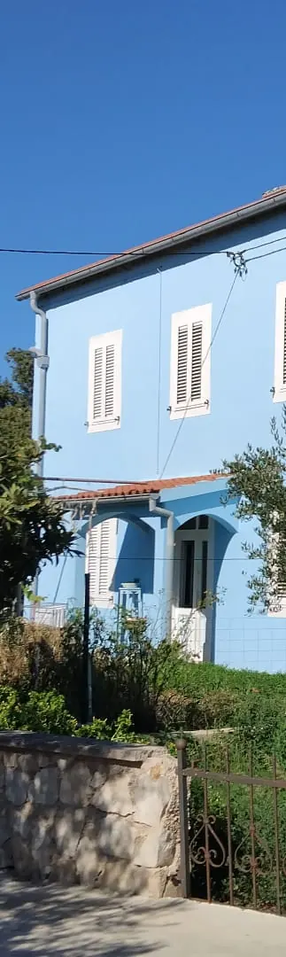 Blue House on Olib: blue façade with white shutters behind a stone garden wall