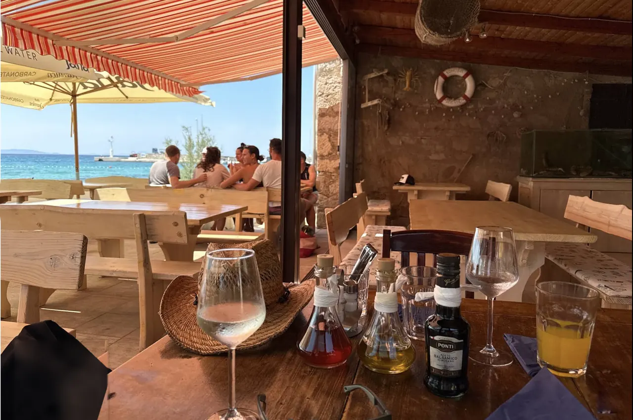 Shaded konoba terrace with wine glasses and olive oil on a wooden table, the sea behind