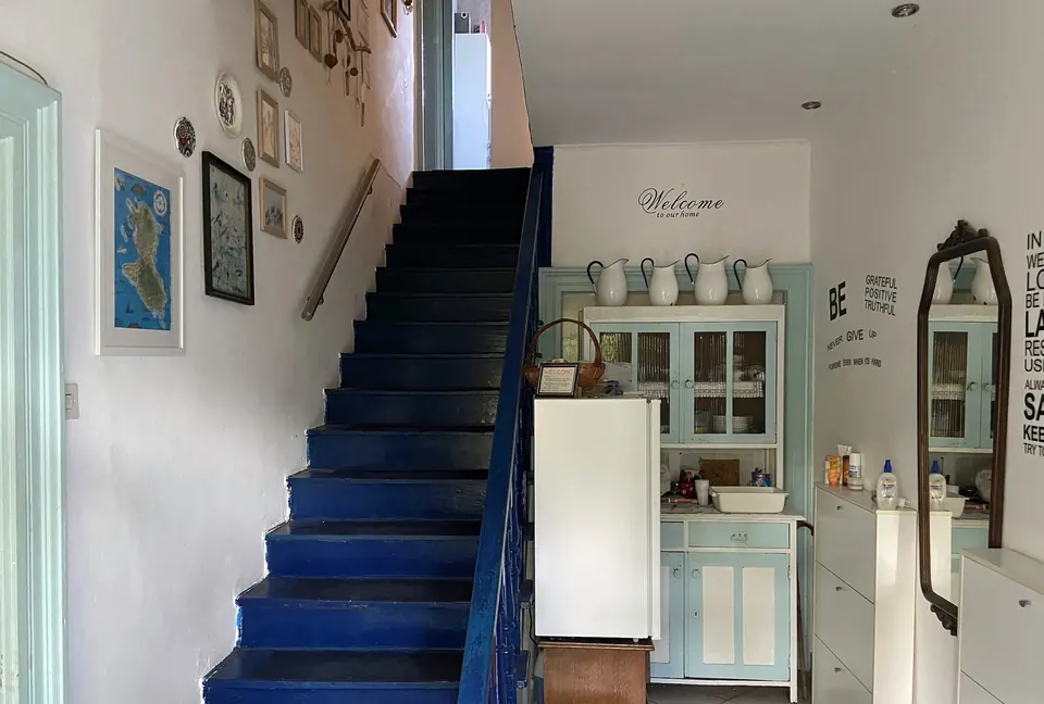 Blue-painted staircase next to a small shared kitchenette with a fridge and a mint-green dresser