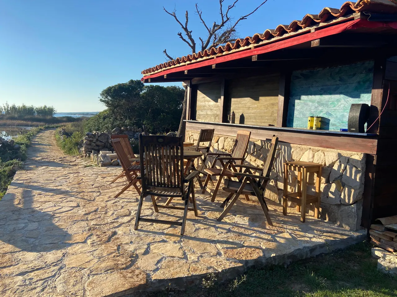 Stone terrace with wooden chairs and a small bar by the sea path