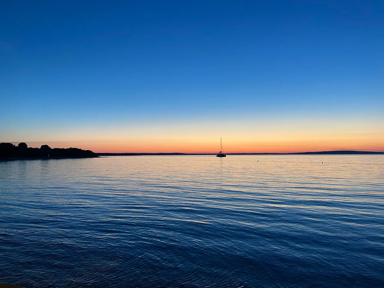 Calm sea at sunset with a lone sailboat on the horizon